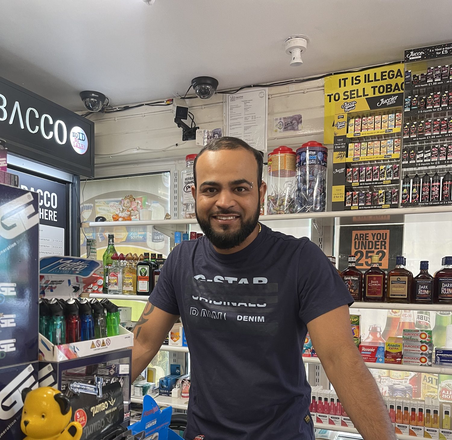 James behind the counter of his convenience store in East London